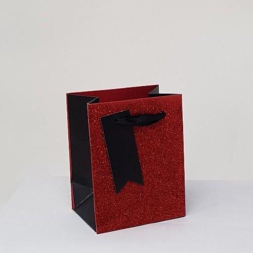 Red glitter perfume gift bag with black sides and ribbon handle.