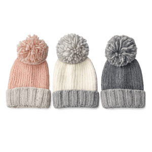 Three knitted winter pom pom hats in pink, cream and grey with chunky ribbed cuffs and soft fluffy pom poms.